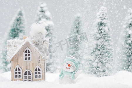 童话的背景摄影照片_小装饰雪人附近的木屋在冷杉林下落雪。冬天的雪人和房子