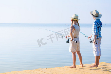 拿着钓鱼竿的男孩和女孩。男孩和女孩拿着钓竿在码头上一起钓鱼