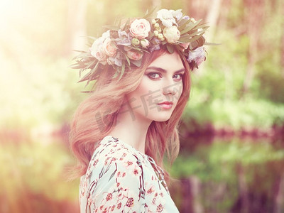 写真女摄影照片_美丽的金发女人头上戴着花环。留着鲜花发型的美女。夏日森林里的女孩。时尚写真
