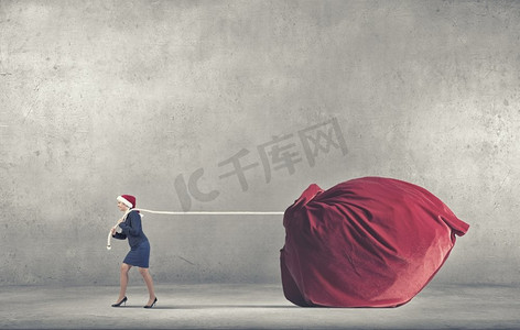 圣诞老人送礼物的女人。戴着圣诞帽的女人拉着巨大的红色礼物包