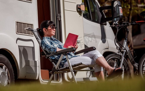 一名女子在露营附近放松地看书。大篷车度假。家庭度假旅行，开着房车度假旅行。