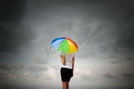 撑伞背影摄影照片_撑着伞的女商人。穿着西装、撑着五颜六色雨伞的女商人的背影