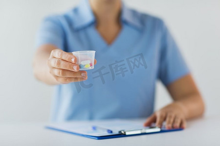 医学、保健和人的概念-护士或医生拿着药丸在医疗杯和剪贴板上。医生拿着药丸在医疗杯里的特写