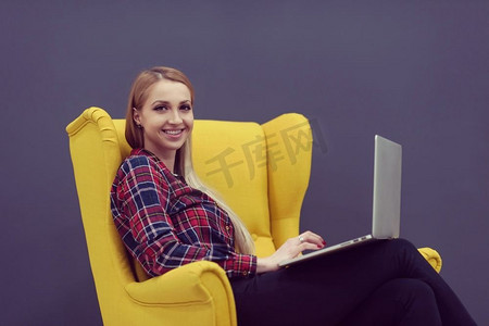 初创企业，在现代办公室用笔记本电脑工作的女人，坐在有创意的黄色扶手椅上