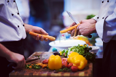 厨师餐厅摄影照片_厨师在一张木桌上切胡萝卜，准备在餐厅就餐。厨师亲手切胡萝卜