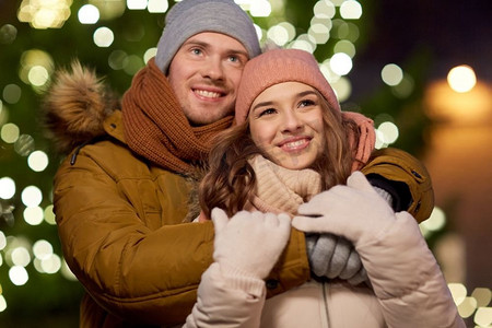 寒假和人们的概念-幸福的年轻情侣晚上在圣诞树前约会和拥抱。幸福的情侣在圣诞树前拥抱