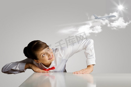 空姐。一名年轻女子俯身在桌子上方，看着天空中的飞机
