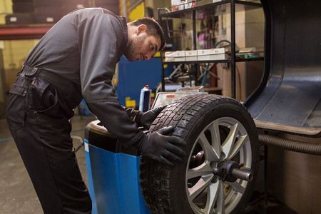 汽车服务、修理、维护和人概念-汽车机械师平衡在车间的人轮胎。汽车机械平衡车轮胎在车间