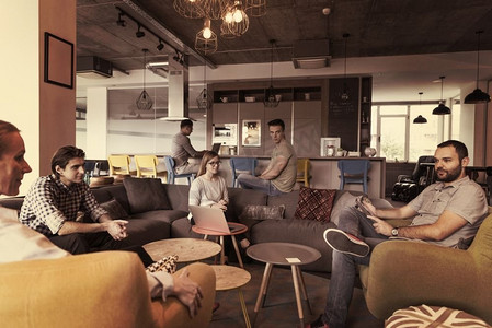 中老年群体摄影照片_现代办公室里的年轻人群体一边工作着笔记本电脑，一边喝着咖啡，举行团队会议和头脑风暴