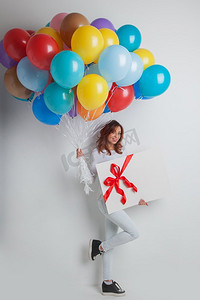 丝带气球摄影照片_带着气球的快乐女人。拿着许多五颜六色的气球和礼盒的快乐女人