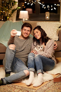 休闲、科技和人的概念幸福的夫妇和猫在家里用智能手机自拍。幸福夫妻在家中用智能手机自拍