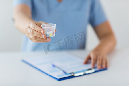 医学、保健和人的概念-护士或医生拿着药丸在医疗杯和剪贴板上。医生拿着药丸在医疗杯里的特写