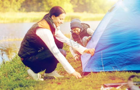 旅游、徒步旅行和家庭概念-快乐的母子在户外搭帐篷。快乐的母子在户外搭帐篷