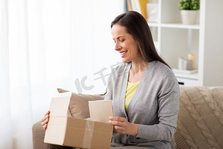 打开的快递盒摄影照片_快递，邮件和人的概念-微笑的女人在家里打开纸箱。微笑的女人打开纸箱