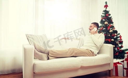 圣诞节，科技，人和节日的概念-微笑的男人在家里用智能手机打电话。一名男子在家里用智能手机过圣诞节