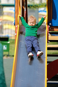 户外学步儿童的肖像。一岁男婴在操场滑梯上穿着绿色毛衣