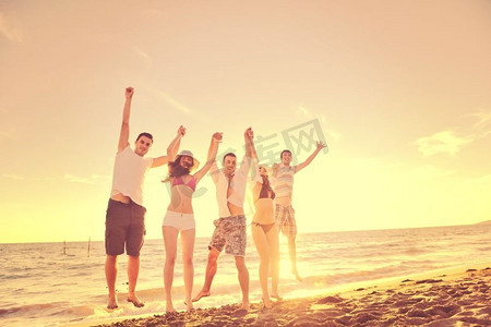 夕阳西下，欢乐青年朋友团在沙滩上跳跃奔跑，尽情玩乐庆祝