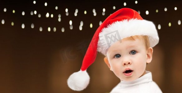 圣诞节，节日和人的概念-戴着圣诞帽的小男婴在花环灯的背景下。圣诞节戴着圣诞帽的小男婴