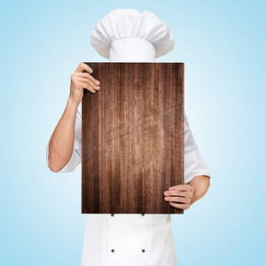 一位餐厅厨师躲在一块木质砧板后面，准备一份商务午餐菜单，上面写着价格。