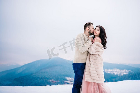 未婚夫摄影照片_穿着毛皮大衣的新娘和未婚夫在喀尔巴底山脉之间