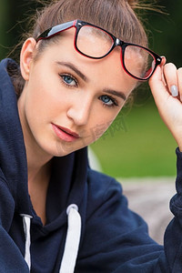戴着眼镜的漂亮聪明的女孩或年轻女子，举起眼镜，露出她的蓝眼睛