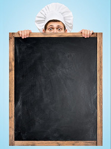 午餐广告摄影照片_一位餐厅厨师躲在一块巨大的空黑板后面，准备一份商务午餐菜单，上面写着价格。