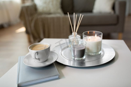 hygge和芳香疗法概念—咖啡，蜡烛，书和香气芦苇扩散在家里的桌子上。咖啡，蜡烛和香味芦苇扩散在桌子上