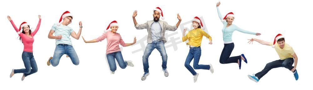 圣诞节、节假日和人们概念快乐的朋友们戴着圣诞帽在空中跳跃。戴着圣诞老人帽子的快乐的人在空中跳跃