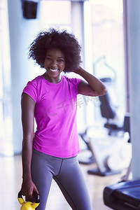 快乐健康的非裔美国女性在CrossFit健身房用哑铃减肥。一名女子戴着哑铃在CrossFit健身房锻炼