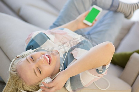 躺在沙发里的女孩摄影照片_年轻漂亮的女孩戴着耳机享受音乐，躺在家里的沙发上