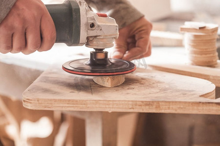 用电额度摄影照片_木匠用电动砂光机打磨木头的地方，工人在打磨木桌。木材磨光机