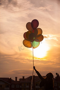 活动大气球摄影照片_美丽的女孩带着五颜六色的大气球走在小镇附近的山上。把注意力放在气球上。拿着五颜六色气球的女孩