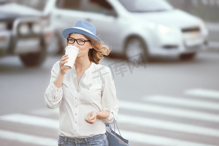 快乐的年轻时髦的学生喝着热的外卖咖啡，在城市的背景下过马路。