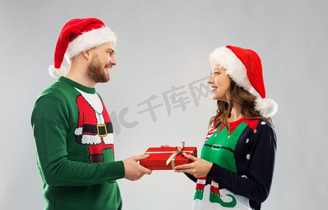 人和假日概念—快乐夫妇在圣诞老人帽子与圣诞礼物在丑陋的毛衣党。快乐的夫妇在圣诞毛衣与礼品盒