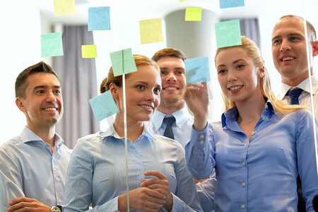 商业和人民的概念-在玻璃墙旁贴着便条的快乐同事。贴着便签的业务团队在玻璃墙前
