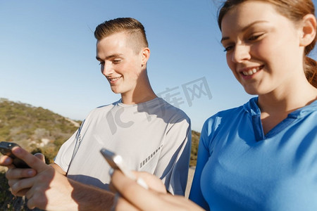 一对年轻夫妇在户外拿着智能手机。两个年轻人在户外穿着智能手机