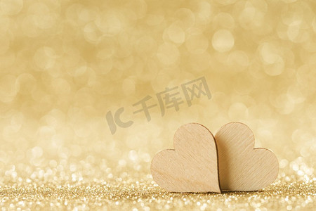 金金色卡摄影照片_在明亮的金色光bokeh背景的两个小手工制作的木心情人节卡。两颗心在散景背景