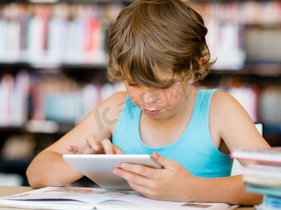 小男孩坐在与平板电脑在图书馆。小学男孩与片剂在图书馆