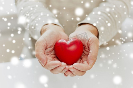 爱、慈善事业和人概念-有红色心脏的资深人关闭在手中在雪关闭高级男子与红心在手