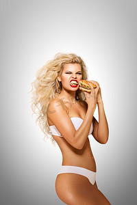 美丽的广告模特在灰色背景下吃着汉堡。