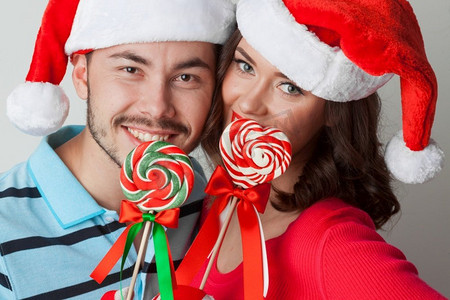 圣诞老人戴着棒棒糖，微笑着的年轻情侣。戴着圣诞老人帽子的情侣