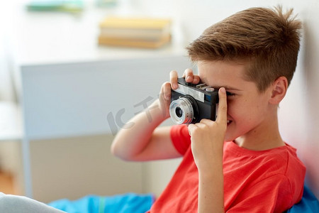 爱好、技术和人概念-有胶片照相机摄影的愉快的男孩在家。快乐的男孩与电影摄影机在家里