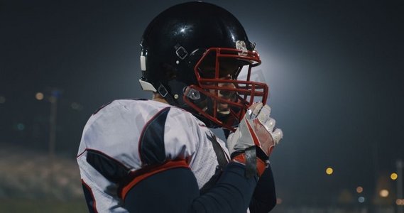 美国橄榄球运动员戴上防护头盔以抵御体育场明亮的照明灯光