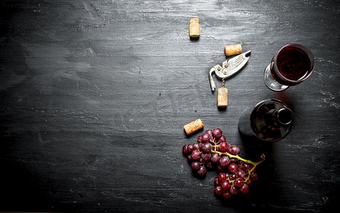 一瓶红葡萄酒和一个开瓶器。在一个黑色的木背景。一瓶红葡萄酒和一个开瓶器。
