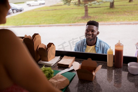 订购弹窗摄影照片_街头小贩和人们的概念-快乐的非裔美国年轻人在美食车上订购炒锅。一名非洲裔美国男子在美食车上点炒锅