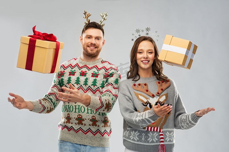 人和假日概念—在丑陋毛衣党的快乐夫妇的肖像与圣诞礼物。快乐的夫妇在圣诞毛衣与礼品盒