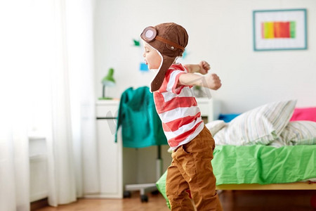 童年，想象力和梦想的概念--快乐的小男孩戴着飞行员帽在家玩游戏。戴着飞行员帽的快乐小男孩在家里玩耍