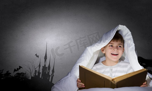 夜色摄影照片_孩子们的噩梦。可爱的小男孩坐在床上，毯子里拿着书