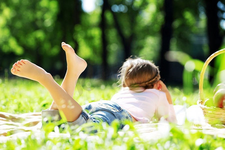 一个孩子躺在毯子上在夏季公园野餐。公园里的女孩