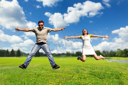 快乐的年轻夫妇跳高在夏季草地。夫妇有乐趣在草地上
